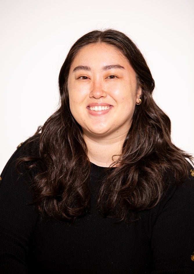 Smiling person with long dark hair wearing a black top against a light background.