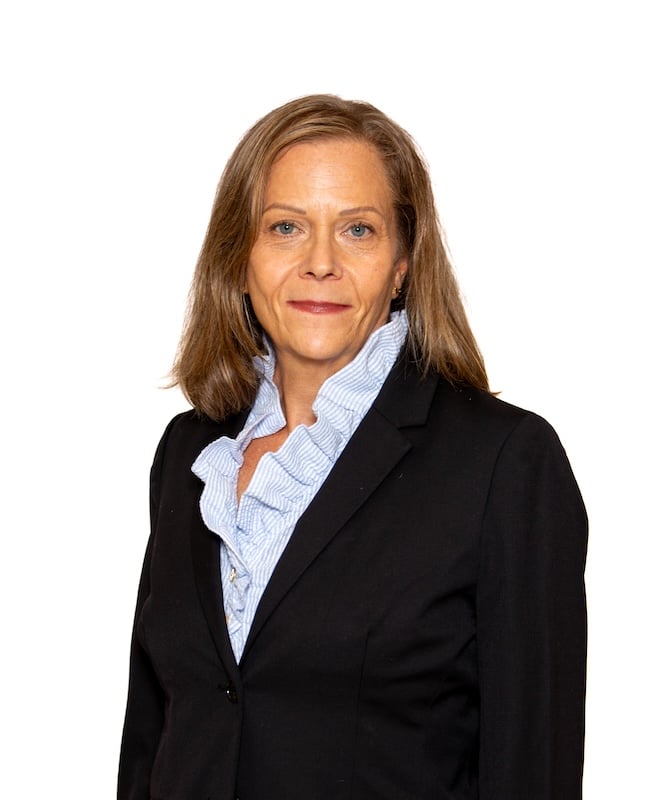 Studio headshot of a woman in a black blazer and light blue ruffled blouse against a white background.