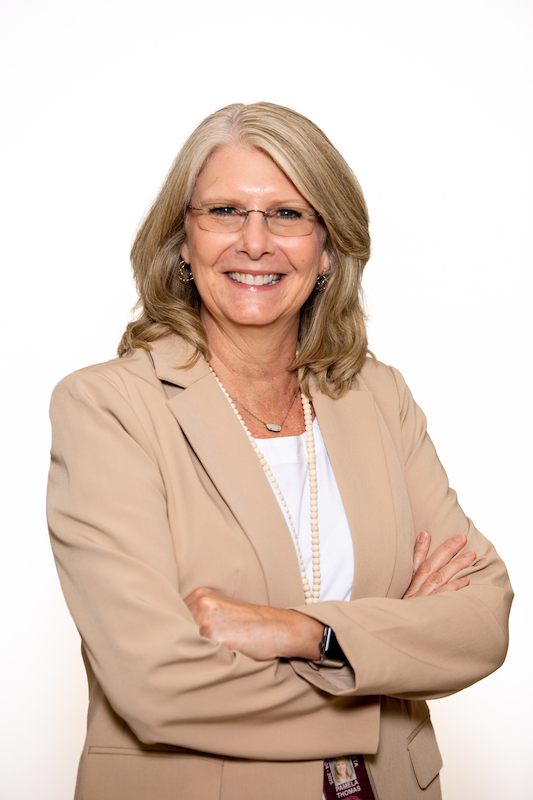Smiling professional woman in a beige blazer and glasses, arms crossed against a white background.